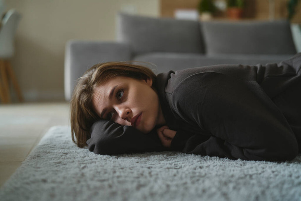 Λευκή γυναίκα ξαπλωμένη στο χαλί στο σπίτι με διανοητικό πρόβλημα  - Φωτογραφία, εικόνα