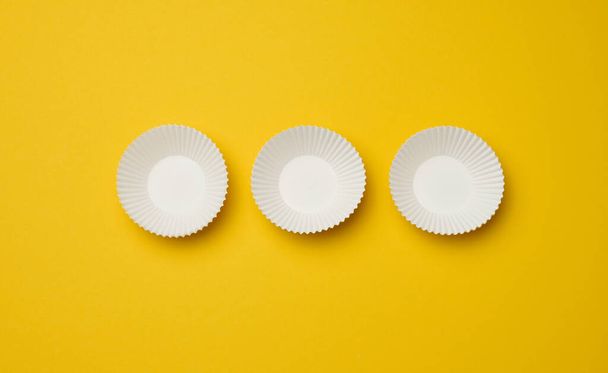 Moldes de cupcake de papel blanco vacíos sobre fondo amarillo, vista superior - Foto, Imagen