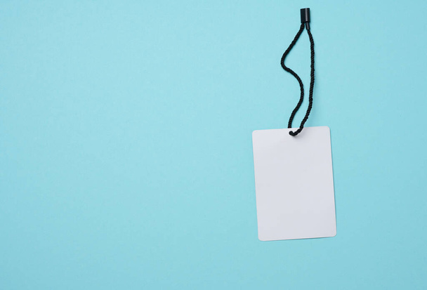 Empty white cardboard tag on a white rope, blue background. Price tag template - Foto, Imagen