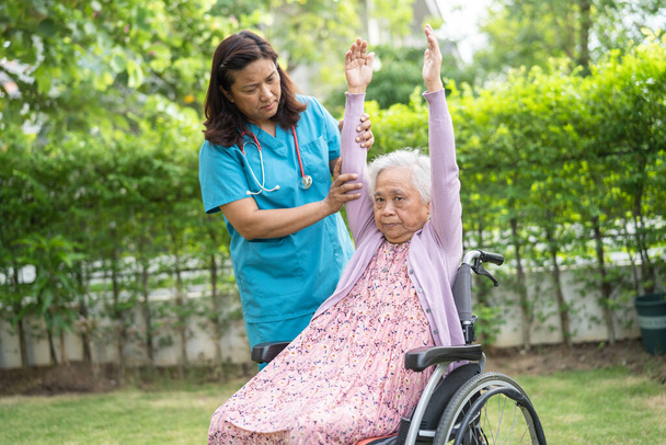 Γιατρός βοηθήσει την ασιατική ανώτερος ή ηλικιωμένη ηλικιωμένη ηλικιωμένη γυναίκα ασθενή άσκηση σε αναπηρική καρέκλα με ευτυχισμένη στο πάρκο. - Φωτογραφία, εικόνα