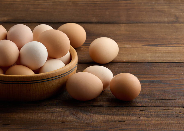 Huevos de pollo marrón fresco en un plato redondo de madera sobre la mesa - Foto, Imagen