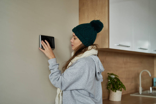 Mujer caucásica usando el panel de control para establecer una temperatura más alta en casa - Foto, imagen