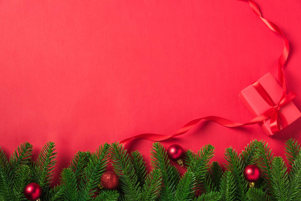 Christmas holiday background with gift box decorations composition, Top view fir green fir tree branches and Xmas ornaments on a red table background - Φωτογραφία, εικόνα