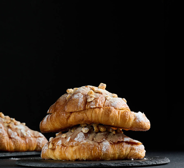 Baked croissant on a  board and sprinkled with powdered sugar, black table. Appetizing pastries for breakfast	 - Fotoğraf, Görsel