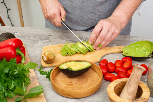 woman's hands preparing avocado to serve. Kitchen table with vegetables and spices, close-up. - Foto, imagen