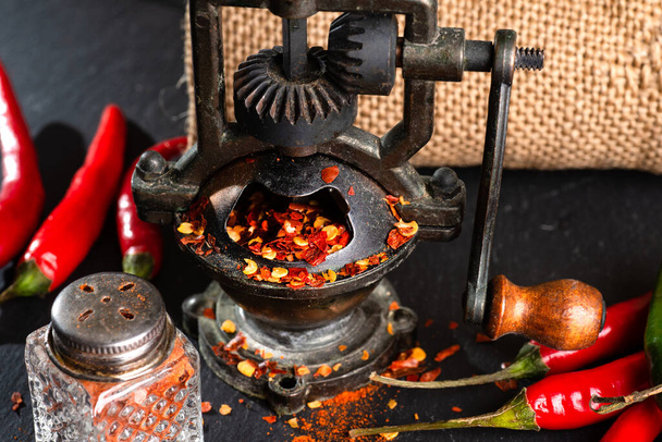 mill and red hot peppers, pepper pods on a black table. - Foto, imagen