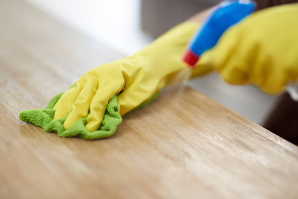 You never know where germ might be lurking. a woman wearing gloves and holding a spray bottle while cleaning a wooden surface at home - Foto, imagen