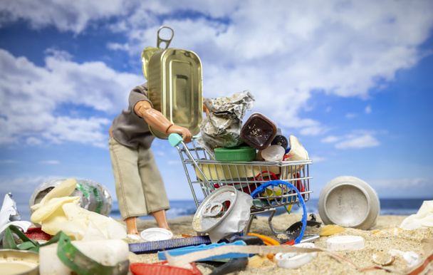 Męska lalka z puszką jako głowa pchająca wózek sklepowy pełen śmieci na plaży  - Zdjęcie, obraz