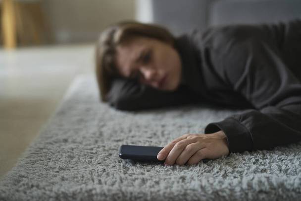 Καυκάσια νευρική γυναίκα ξαπλωμένη στο πάτωμα με κινητό τηλέφωνο - Φωτογραφία, εικόνα