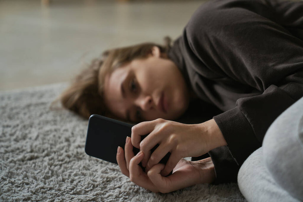 Biała nerwowa kobieta leżąca na podłodze z telefonem komórkowym - Zdjęcie, obraz