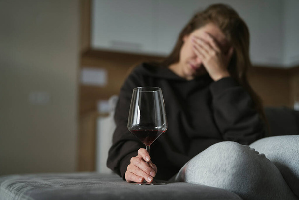 Alkoholista fehér nő ül a kanapén és egy pohár bort tart a kezében.   - Fotó, kép