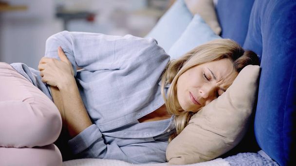 kimerült nő csukott szemmel szenved hasi fájdalom és fekszik az ágyon   - Fotó, kép