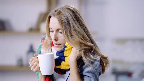 diseased woman in colorful scarf holding cup with tea at home  - Фото, зображення