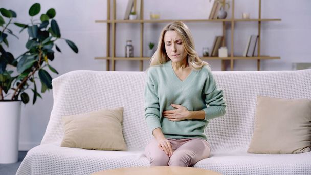 Erschöpfte Frau leidet unter Bauchschmerzen und sitzt auf Couch - Foto, Bild