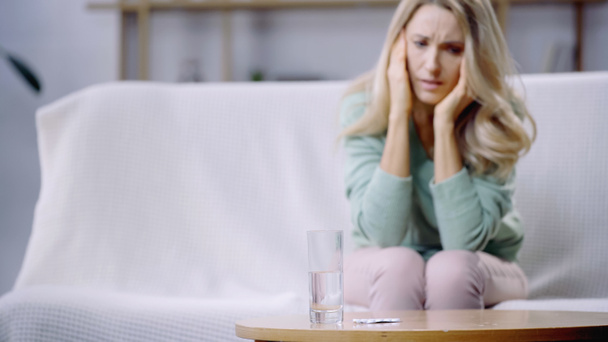 glass of water and pills on coffee table near woman having migraine on blurred background - Photo, image