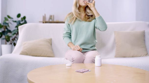 cropped view of woman taking pill and drinking water in living room  - Foto, immagini