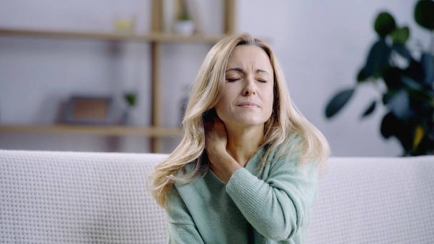sad and blonde woman with closed eyes having pain in neck  - Фото, зображення