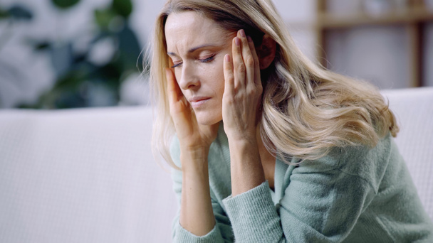femme triste avec les yeux fermés ayant la migraine et touchant la tête dans le salon - Photo, image