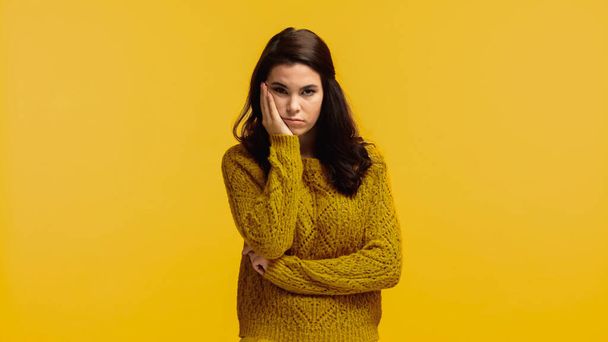 黄色で隔絶された頬に触れるセーターの若い退屈した女性 - 写真・画像