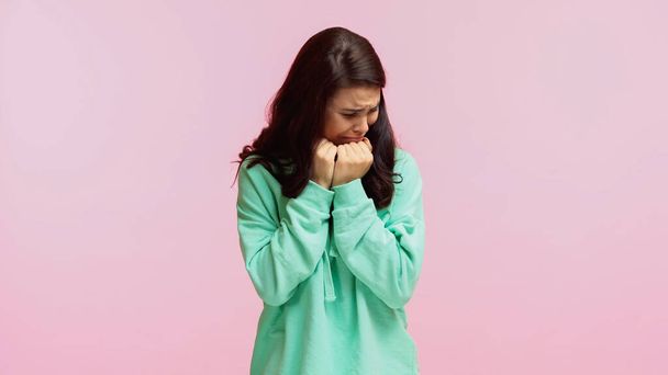 young sad woman in turquoise hoodie crying isolated on pink  - Fotó, kép