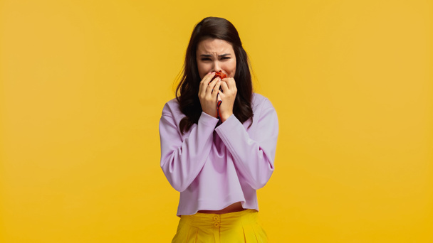 mujer molesta en sudadera púrpura cubriendo la cara mientras llora aislado en amarillo - Foto, Imagen