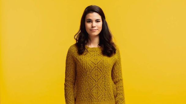 young and brunette woman in sweater looking at camera isolated on yellow - Fotó, kép