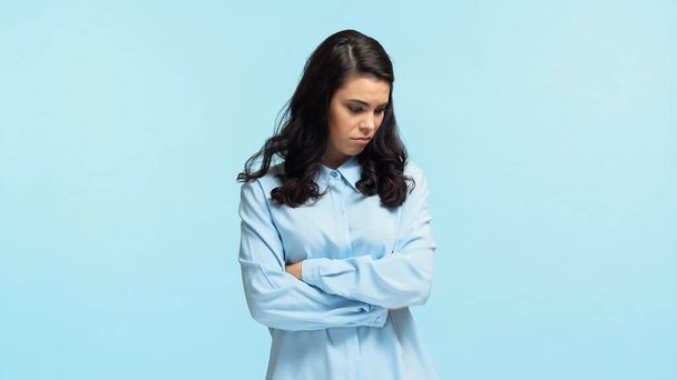 sad young woman in shirt standing with crossed arms isolated on blue - Photo, Image