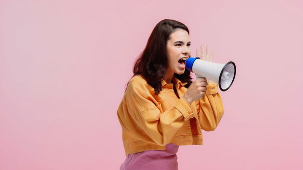 brünette Frau schreit während Durchsage in Lautsprecher isoliert auf rosa - Foto, Bild