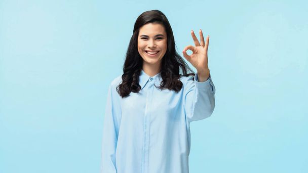 joyful young woman in shirt looking at camera while showing ok isolated on blue - Fotoğraf, Görsel