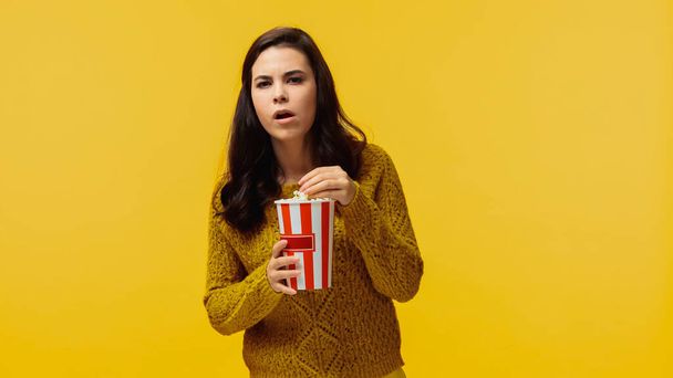 επικεντρώθηκε νεαρή γυναίκα σε πουλόβερ τρώει ποπ κορν και βλέποντας ταινία απομονώνονται σε κίτρινο - Φωτογραφία, εικόνα