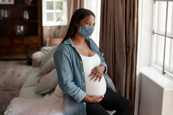 Ciąża była trudnym doświadczeniem podczas pandemii. ciężarna kobieta ubrana w maskę i wyglądająca troskliwie w domu - Zdjęcie, obraz