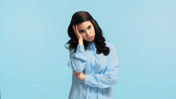 displeased young woman in shirt touching head while puffing cheeks isolated on blue - Foto, Imagem