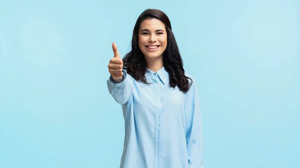 θετική νεαρή γυναίκα με πουκάμισο κοιτάζοντας την κάμερα, ενώ δείχνει τον αντίχειρα προς τα πάνω απομονώνονται σε μπλε - Φωτογραφία, εικόνα