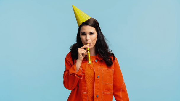 happy young woman in orange jacket and cap blowing party horn isolated on blue - Foto, Bild
