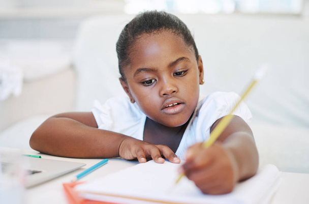 Gericht op het afmaken van huiswerk. een klein meisje dat thuis in een boek schrijft - Foto, afbeelding