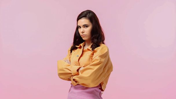 offended young woman in orange jacket standing with crossed arms isolated on pink  - Фото, изображение