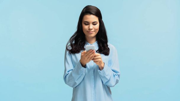 счастливая молодая женщина в рубашке сообщения на смартфоне изолированы на синий - Фото, изображение