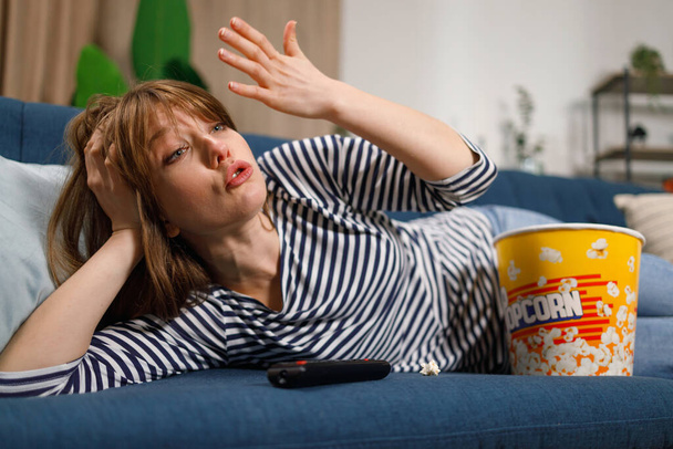 Angry young woman emotionally watching TV at home on sofa - Valokuva, kuva