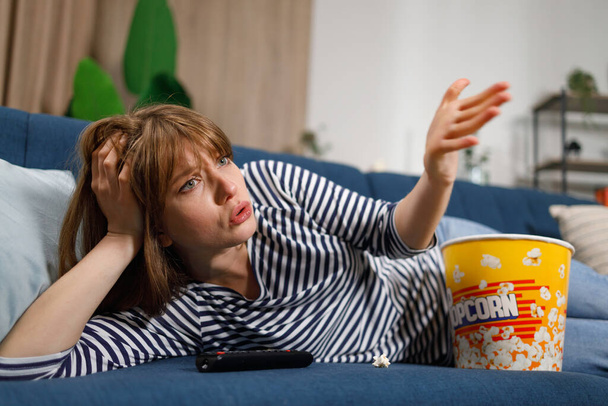 Frustrato donna guardando la TV mentre seduto sul divano in casa - Foto, immagini