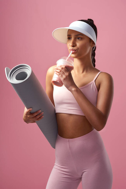 Poštovní občerstvení. atraktivní a sportovní mladá žena pózující s rohožkou na cvičení a smoothie ve studiu na růžovém pozadí - Fotografie, Obrázek