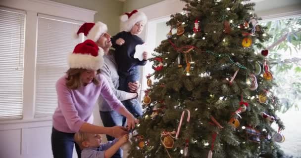 Schöne kaukasische Familie schmückt gemeinsam Weihnachtsbaum - Filmmaterial, Video