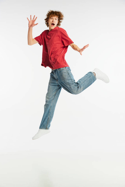 Full length portrait of excited young man jumping, dancing, having fun isolated over white background. Sport, dance, fitness, happiness. Model in casual style clothes in motion at studio shoot - Foto, afbeelding