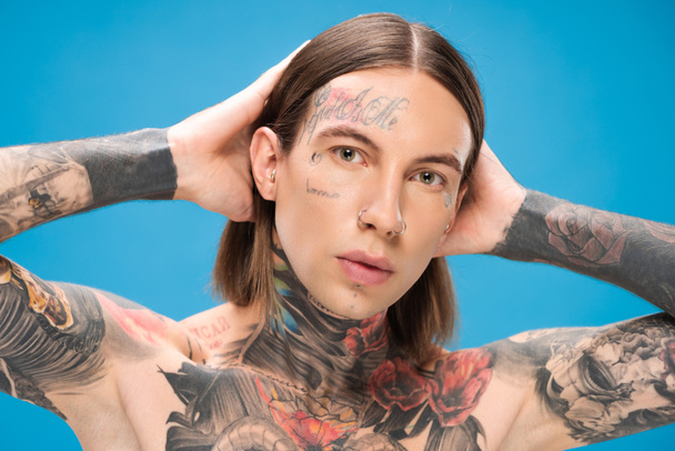 young and pierced man with tattoos looking at camera while posing isolated on blue - Foto, Imagem