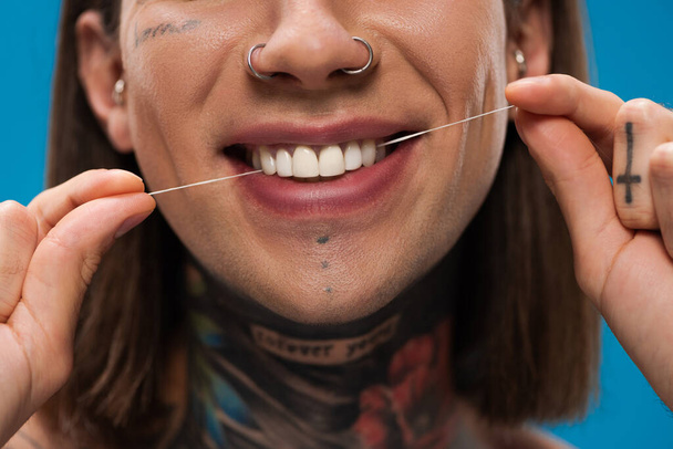 Mavi üzerinde beyaz dişleri olan neşeli ve dövmeli adamın kırpılmış görüntüsü. - Fotoğraf, Görsel