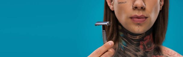 cropped view of young man with tattoos holding safety razor isolated on blue - Фото, изображение