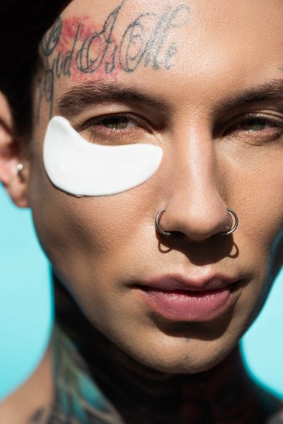 close up of tattooed young man with eye patch looking at camera isolated on turquoise - Photo, Image