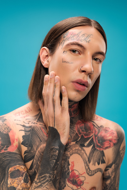 shirtless young man with tattoos looking at camera while touching smooth skin isolated on blue  - Фото, зображення