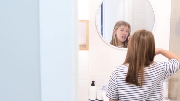 Une adolescente se brosse soigneusement les dents devant le miroir de la salle de bain. Hygiène dentaire des enfants - Séquence, vidéo