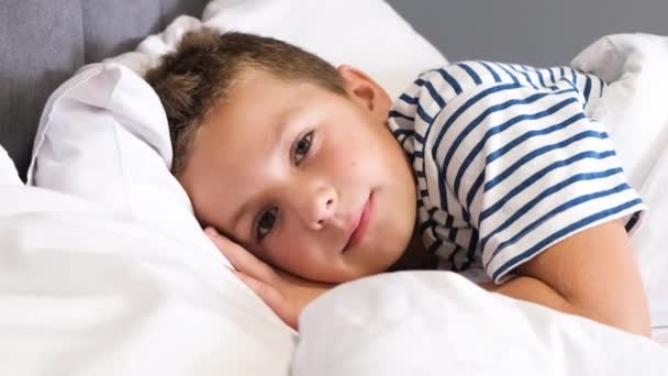 Portrét malého chlapce, jak úhledně leží a usíná na posteli s bílým ložním prádlem. Ráno dospívající kluci. Pohodlný spánek. - Záběry, video