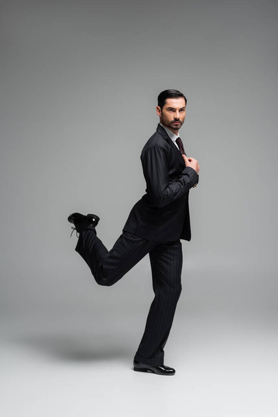Full length of professional dancer moving and adjusting jacket on grey background - Fotografie, Obrázek